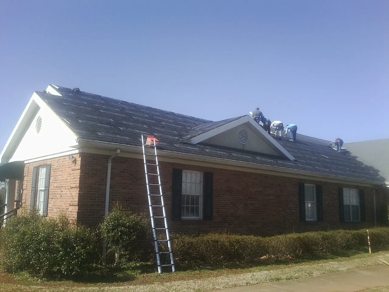 Crew tearing shingles off a brick ranch roof with a ladder set — Emergency Roof Repair work by our crew in Alabaster