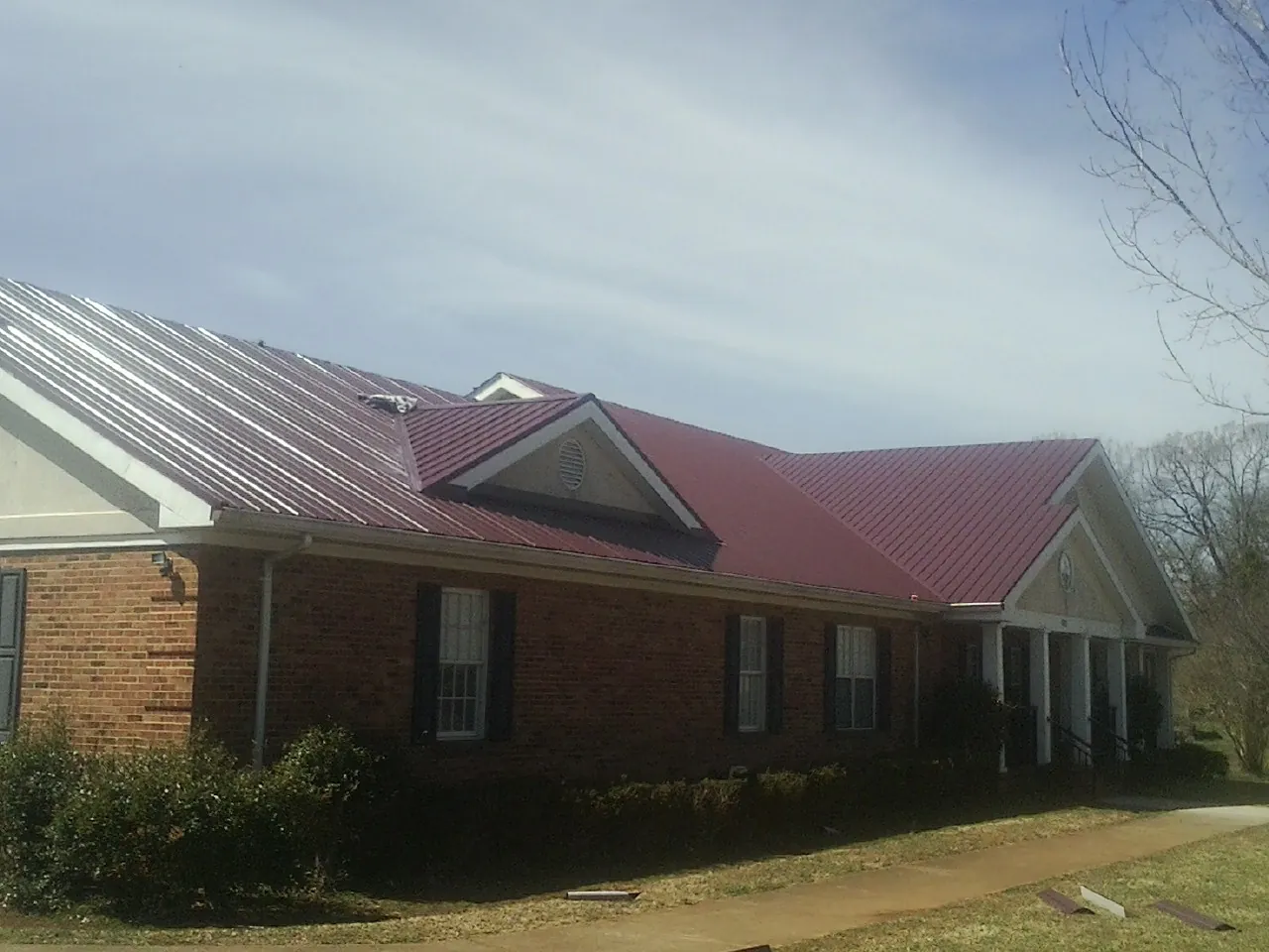 Red metal roof with gabled entries on a long brick building, from a Hail Damage Roof Repair job in Alabaster