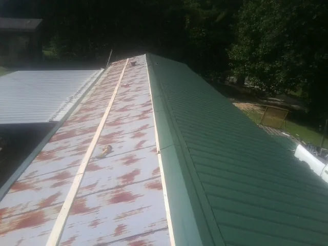 Old rusted panels beside newly installed green metal roofing — Wind Damage Roof Repair by Roofing Brothers in Alabaster