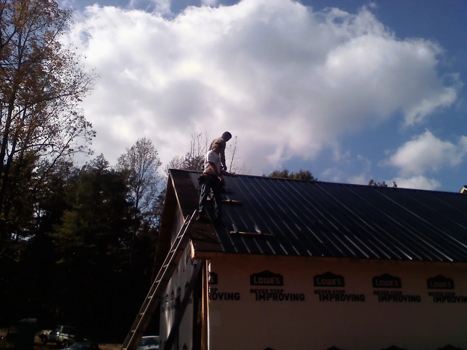 Roofer fastening dark metal panels high against a cloudy sky, from a Roof Inspection job in Alabaster