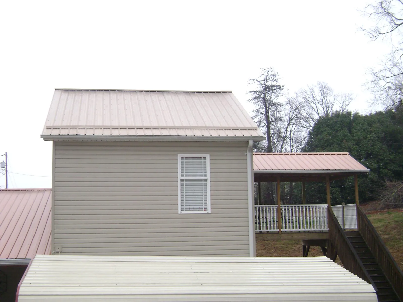 Tan metal roofs on a two story addition and attached porch, from a Roof Replacement job in Alabaster